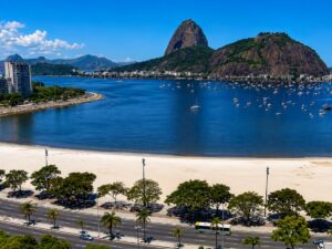 Vista panorâmica da curva da Enseada de Copacabana com o mar azul, areia clara e prédios da orla ao fundo sob céu limpo