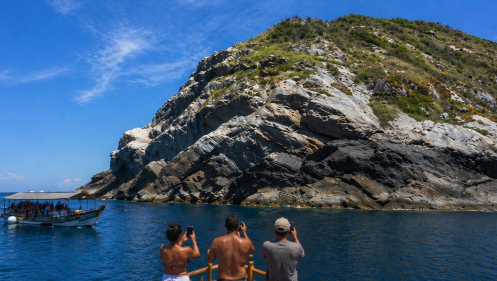 Turistas na proa de barco observando a Pedra do Macaco em Arraial do Cabo com mar azul e formação rochosa